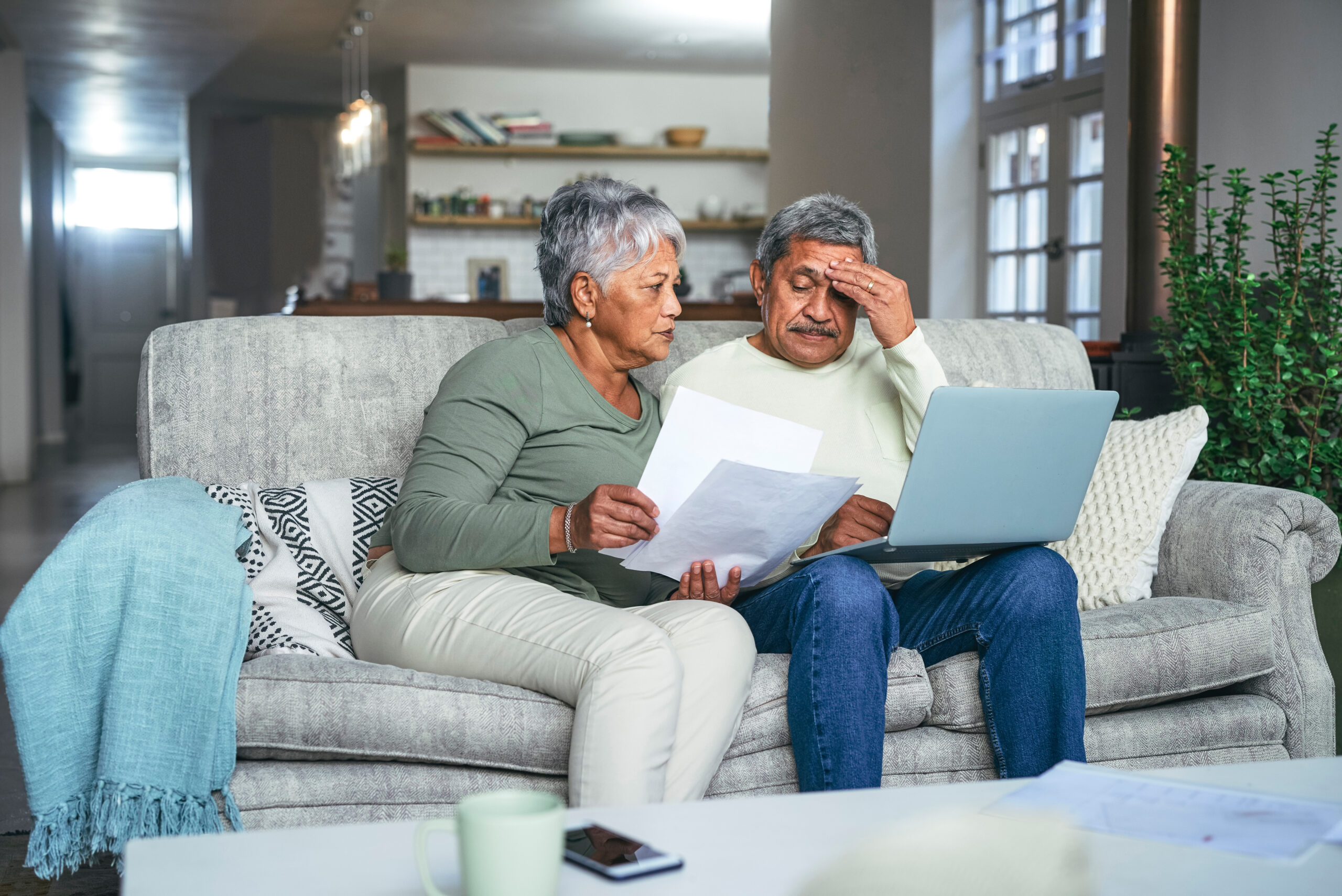 A man and woman sitting on the couch looking at papers.